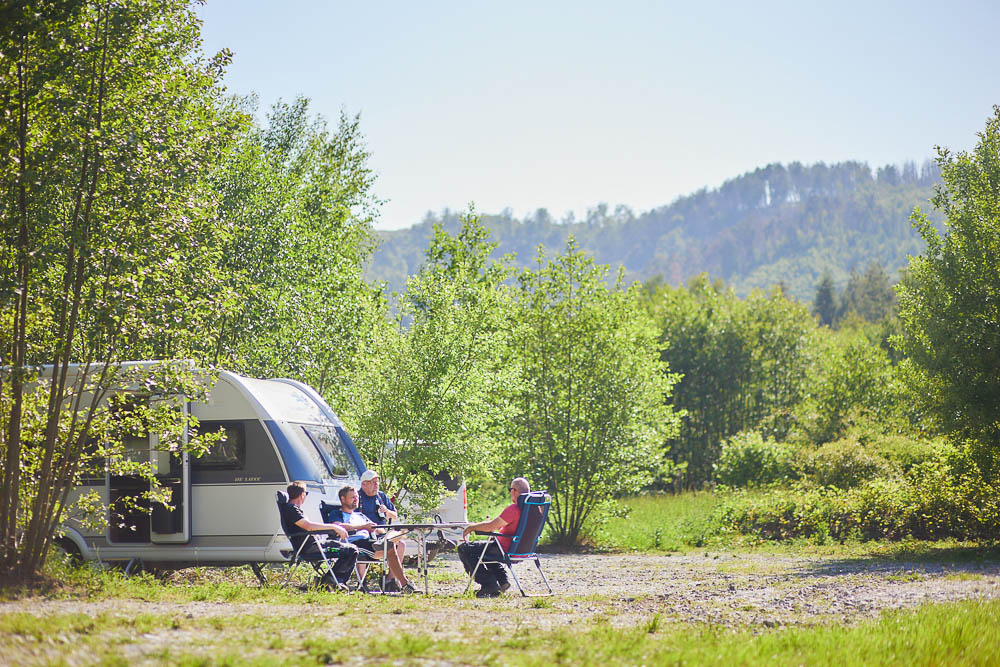 Einige Männer auf Campingstühlen auf dem Ein Wohnmobil auf dem Wohnmobilstellplatz im Ilsenburger Sandtal im Harz.